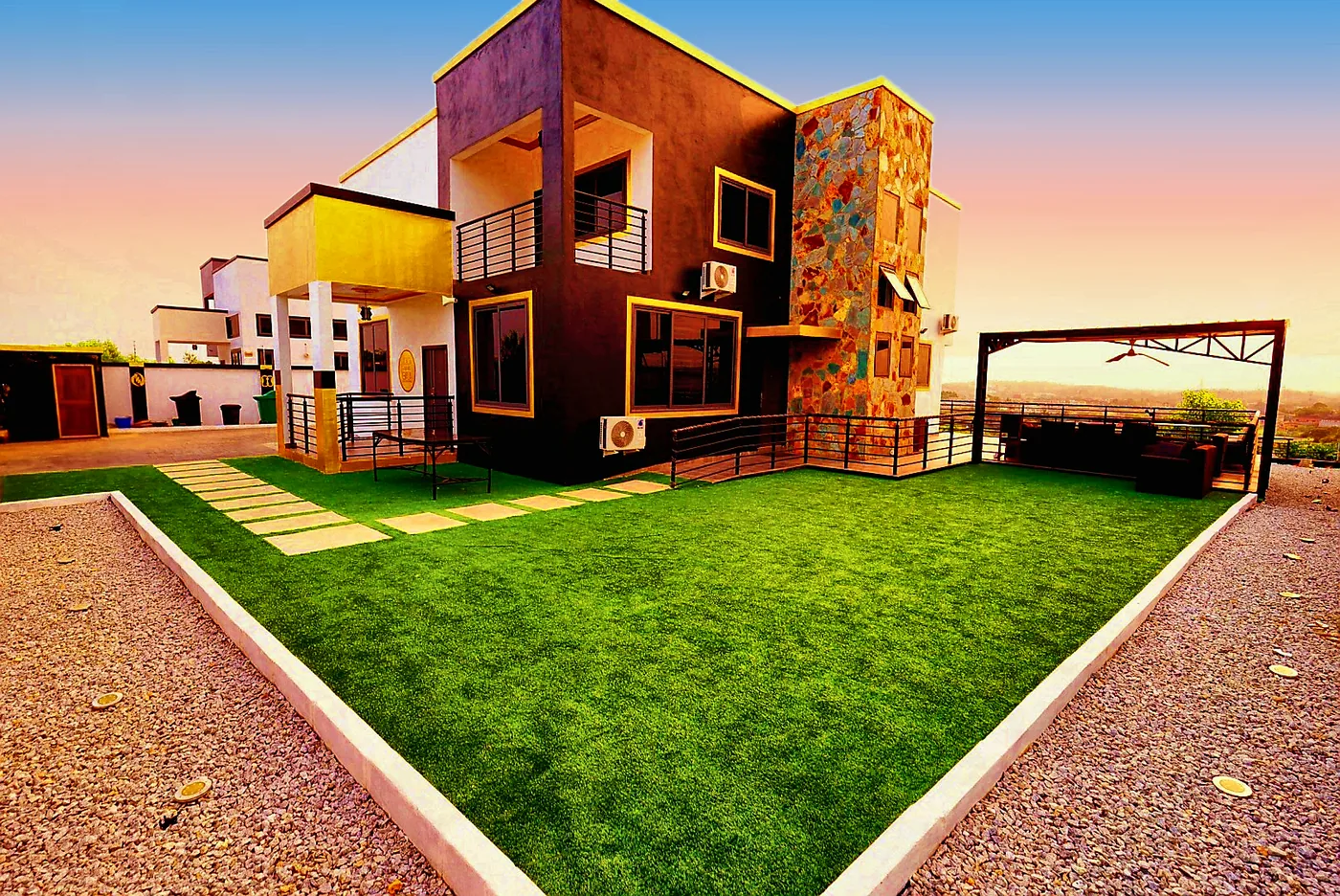 The finished two-story Cape Coast center in brown, white and gold with a stone tower, green lawn and covered terrace at sunset